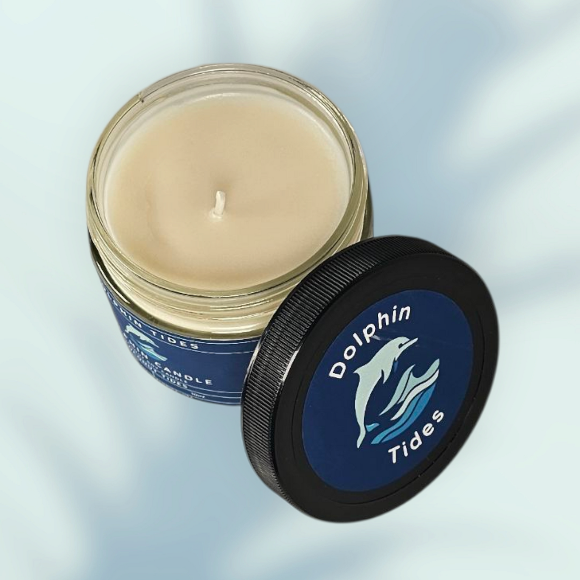 Candle in a jar with a blue label featuring a dolphin and 'Dolphin Tides' branding on a light gray background.