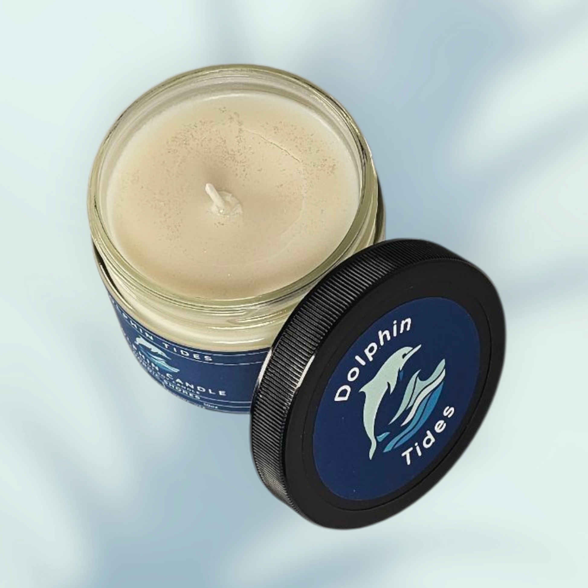 Candle in a jar with a black lid featuring 'Dolphin Tides' branding on a light blue background.