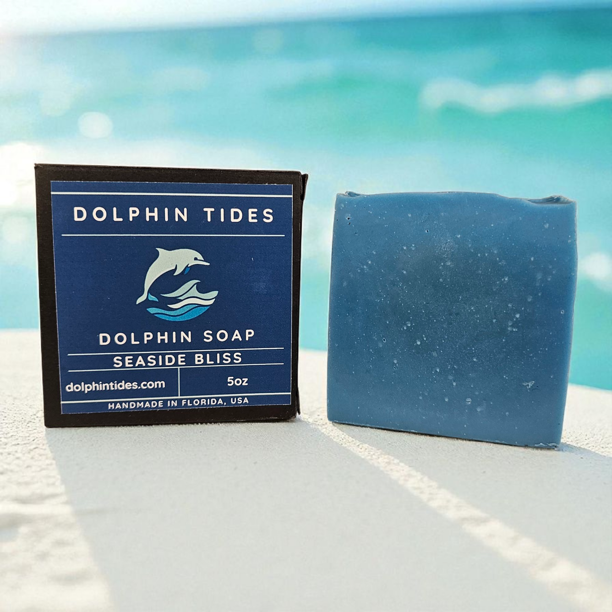 Blue soap bar and packaging with 'Dolphin Tides' branding on a beach.