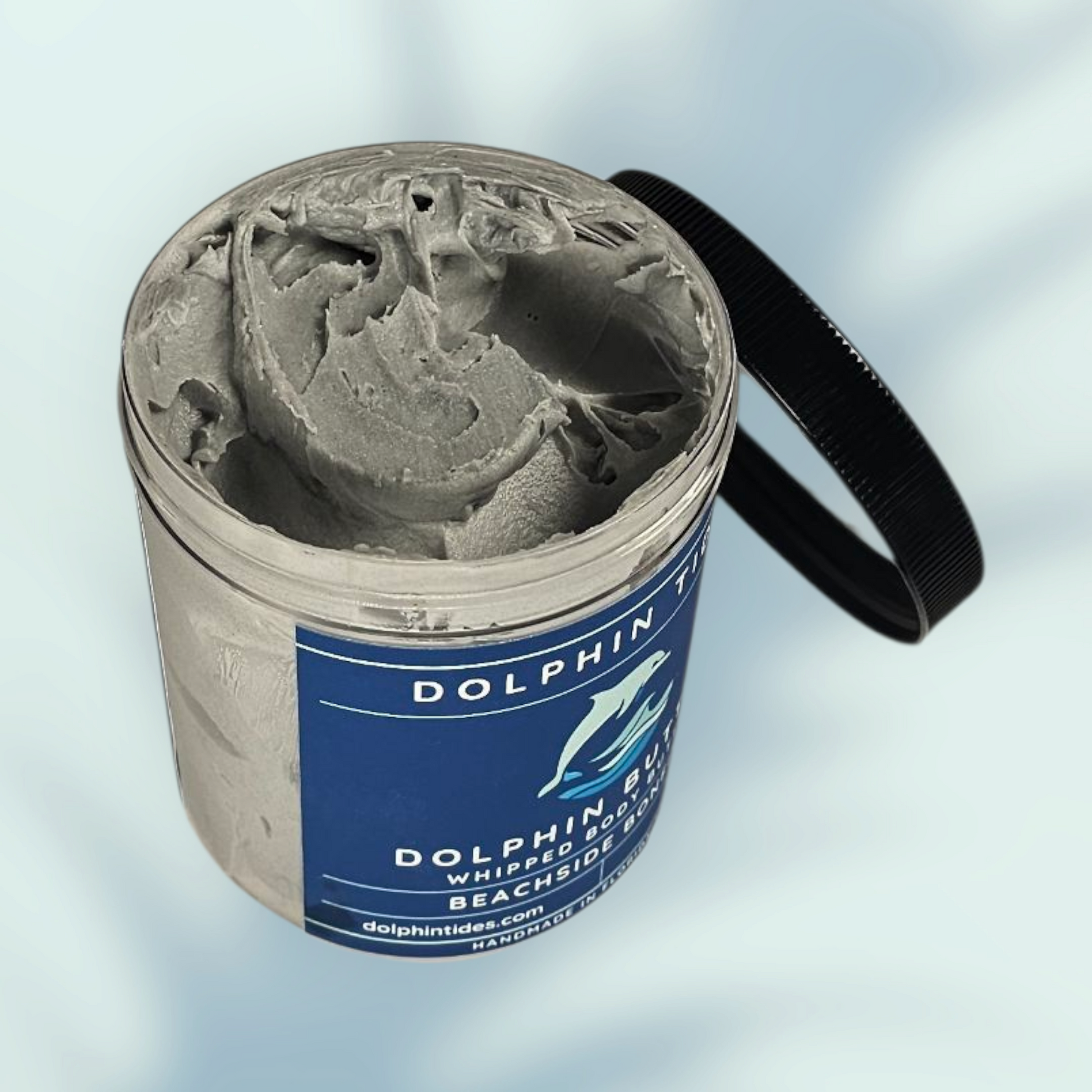 Dolphin Tides whipped body scrub in a container with a blue label on a light gray background