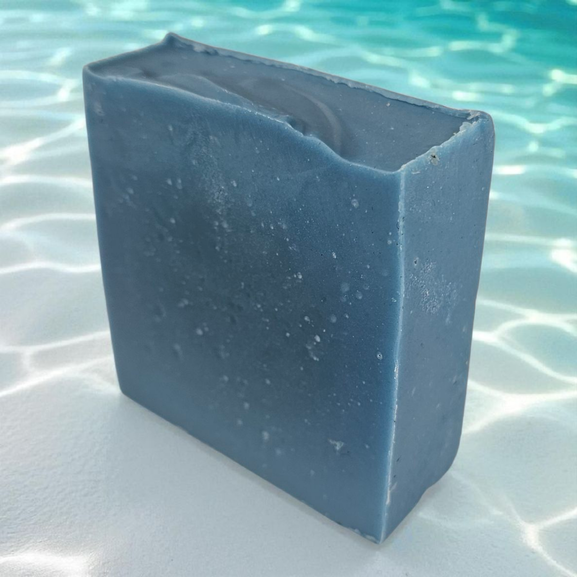 Blue rectangular block of soap on a white surface with water in the background