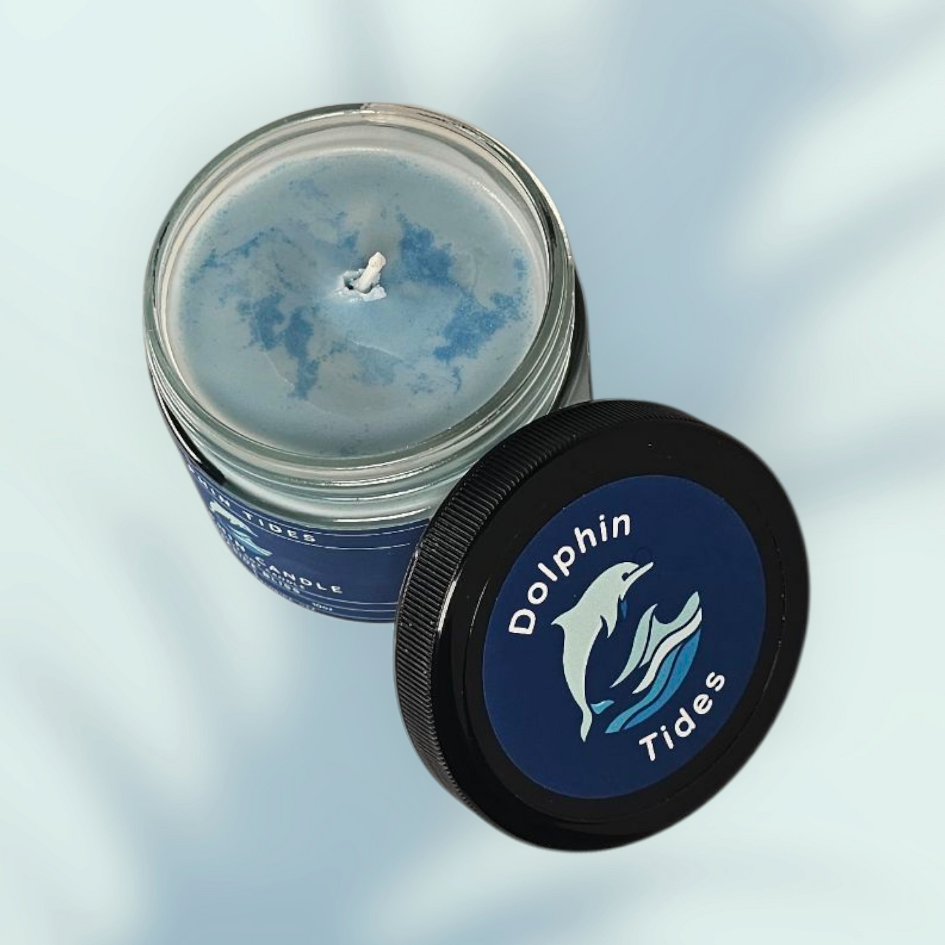 Candle in a jar with a blue label featuring a dolphin design on a light gray background