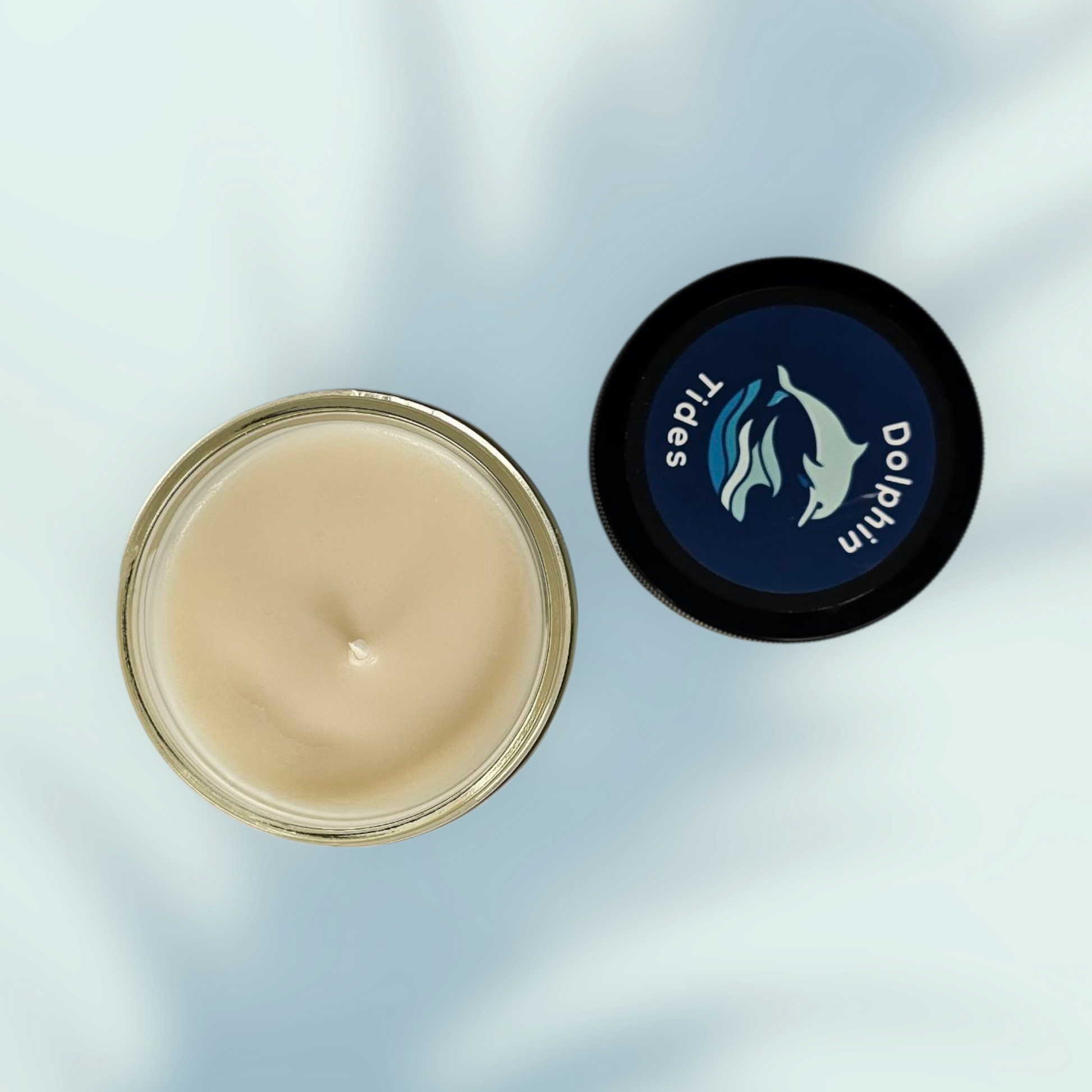 Jar of cream with a black lid featuring a dolphin design on a light blue background