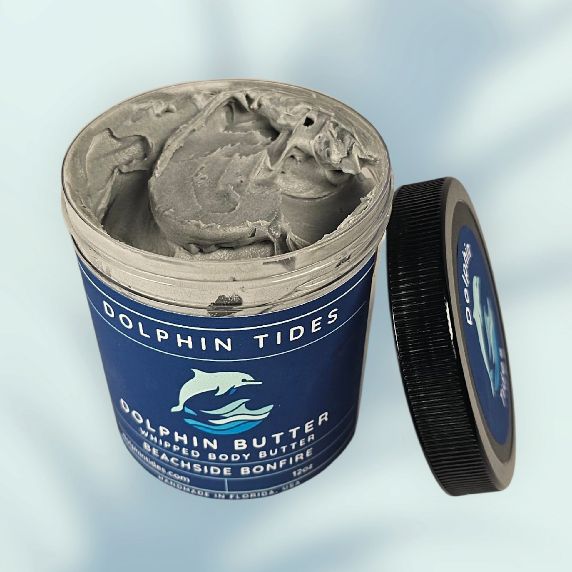 Dolphin Tides whipped body butter container with open lid on a light blue background